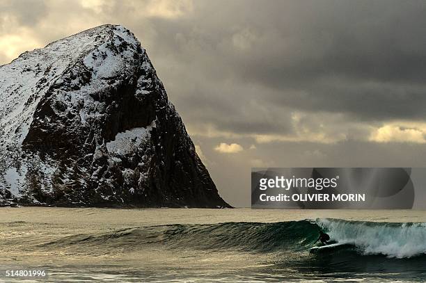 Surfer rides a wave at the snowy beach of Unstad, in Lofoten Island, Arctic Circle, on March 10, 2016. Surfers from all over the world comes to...