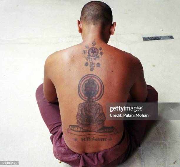 Young Buddhist monk with a tattoo of Buddha on his back sits outside the entrance to the Thamkrabok Monastery October 5, 2004 in Lopburi, Thailand....
