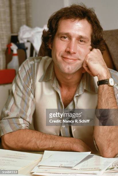American actor and comedian Chevy Chase rests his head on his fist while seated at a desk covered with paperwork, 1979.
