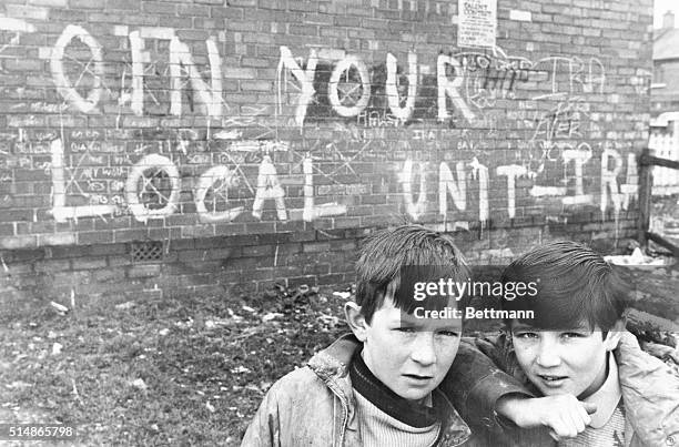 Two boys play near a graffitied wall inscripted: "Join your local unit-IRA," common evidence of support for the local Irish Republican Army in...