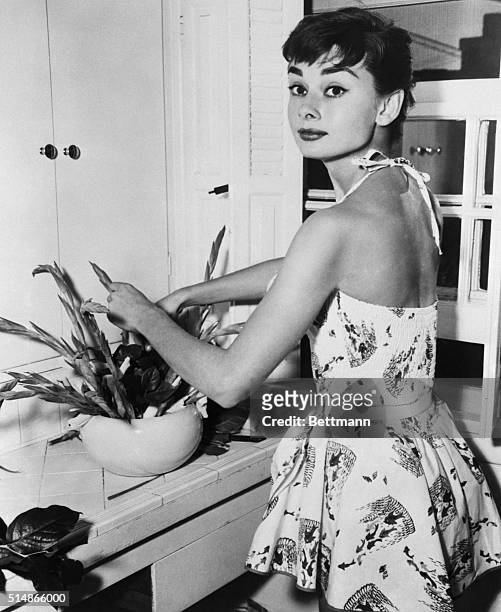 New York, NY: Pixyish Audrey Hepburn, Academy Award actress, beats the Manhattan heat with a cool play suit as she does chores in her New York...