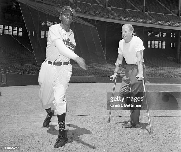 Cleveland Indians owner Bill Veeck, Jr., standing on crutches, watches pitcher Satchel Paige warm up.