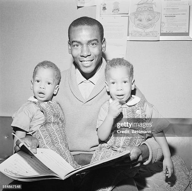 Chicago Cubs' star shortstop Ernie Banks reads a story to his two-year-old twin sons, Joel and Jerome, as they wait at the doctor's office to see the...