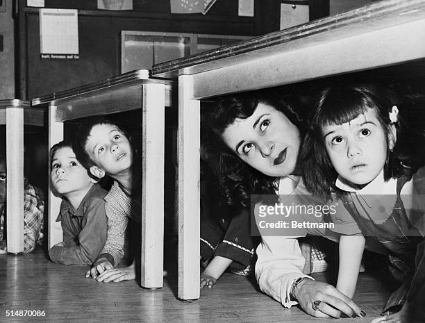 Newark, NJ: School children and their teacher peer from beneath the table where they took refuge at Lafayette Street School when the sirens howled...