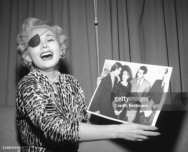 Las Vegas, NV: "Look how unhappy they both look!" Zsa Zsa Gabor laughs as she is handed a United Press Telephoto of the Porfirio Rubirosa and Barbara...
