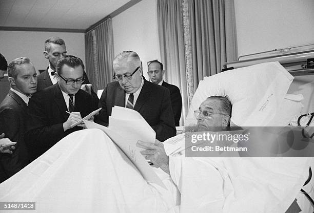 Bethesda, Maryland: With newsmen standing beside him, President Johnson looks over some documents in his hospital bed, November 16th, after...