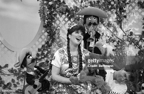 Linda Ronstadt and popular muppet Elmo sing with mariachi style muppets on Sesame Street. A puppeteer moves Elmo from just out of camera range.