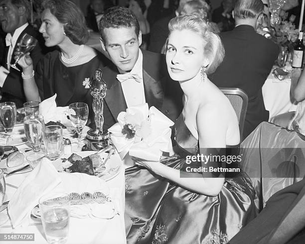 Joanne Woodward, named best actress for her role in The Three Faces of Eve, sits at a dinner table with her husband, Paul Newman, with her Oscar...