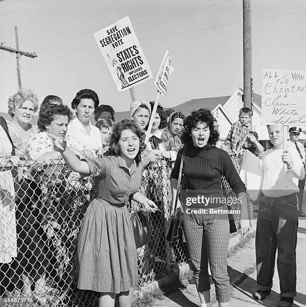 Women at William Franz Elementary School yell at police officers during a protest against desegregation at the school, as three black youngsters...