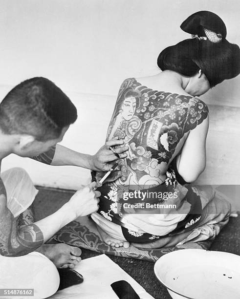 Tokyo, Japan: In defiance of the law, many Japanese go in heavily for tattooing. Here an expert imprints his weird designs on the body of a woman....