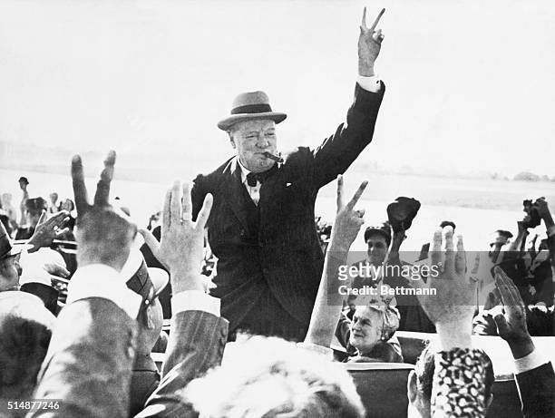 Sir Winston Churchill makes the Victory Sign as he greets well-wishers from his automobile. Photograph.