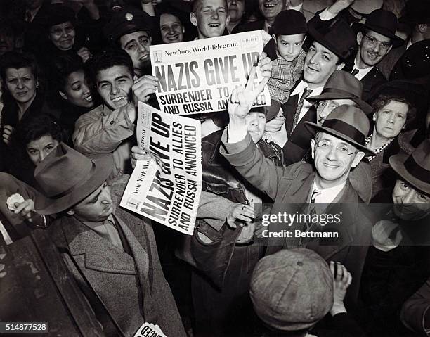 Celebrations begin in New York on the announcement of Germany's surrender at the end of World War II, 7th May 1945. People are holding up copies of...