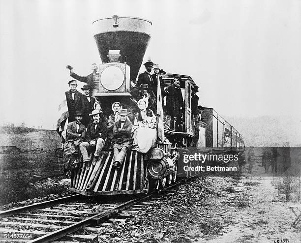 Photograph of the first locomotive to cross the Allegheny Mountains. Passengers ride the cowcatcher.