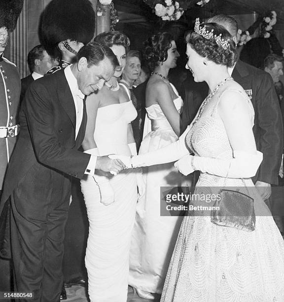 London, England: Entertainer Frank Sinatra bows as he is presented to smiling Queen Elizabeth at movie premiere here, Oct. 27. The film being shown...