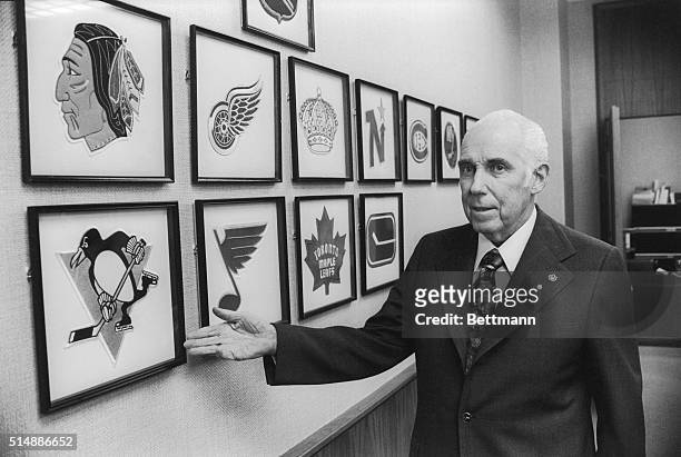 National Hockey League President Clarence Campbell looks over some of the team crests in his office.