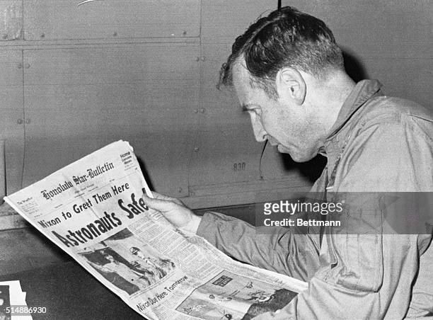 Apollo 13 astronaut James Lovell reads the headlines chronicling his safe return frm space as he rides an Air Force plane from Pago Pago to here...