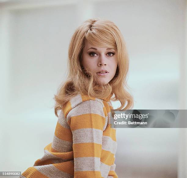 Young Jane Fonda in a waist length shot poses in a mustard yellow sweater.