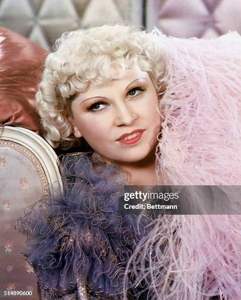 Close-up of actress Mae West. She is reclining in a pink boa. Undated photograph.