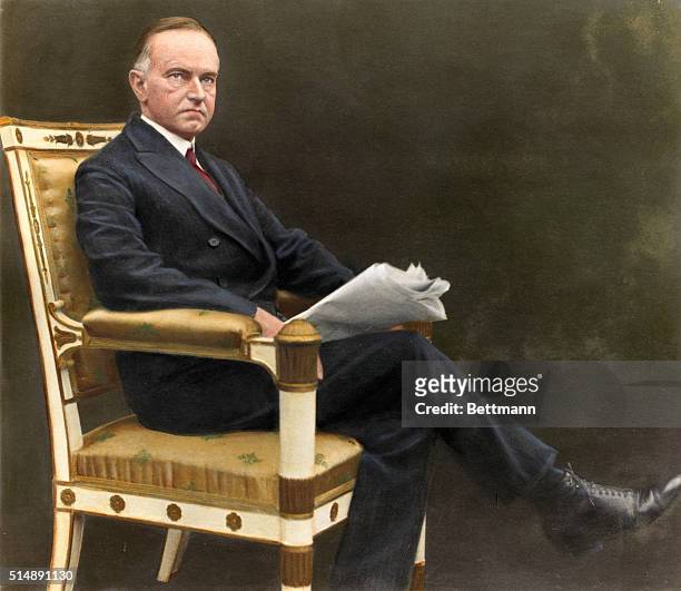 Calvin Coolidge is shown seated, reading a newspaper. Colored photograph, ca. 1920s.