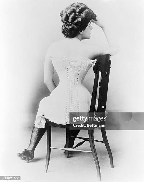 Young lady in victorian corset. Back view seated in chair. Undated photograph.