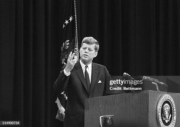 President Kennedy holds up two fingers to indicate that the United States is running second in the space race during his news conference here today....
