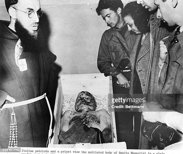 Italian patriots and a priest view the mutilated body of Benito Mussolini in a plain, wooden casket in Milan, 1945.