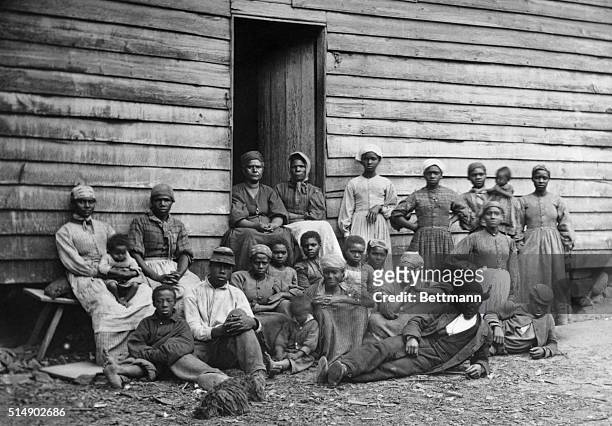 Group of slaves outside their log cabin lodging. Undated photograph.