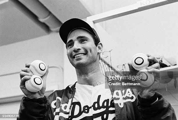 Los Angeles, CA: In the dressing room late 9/9, Dodgers' pitcher Sandy Koufax holds up four balls with zeros on them, one for each of his no-hitters....