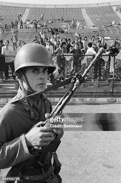 Santiago, Chile- An armed guard watches prisoners of the Chilean Army in the stands of Santiago's National Stadium. The army is using the stadium as...