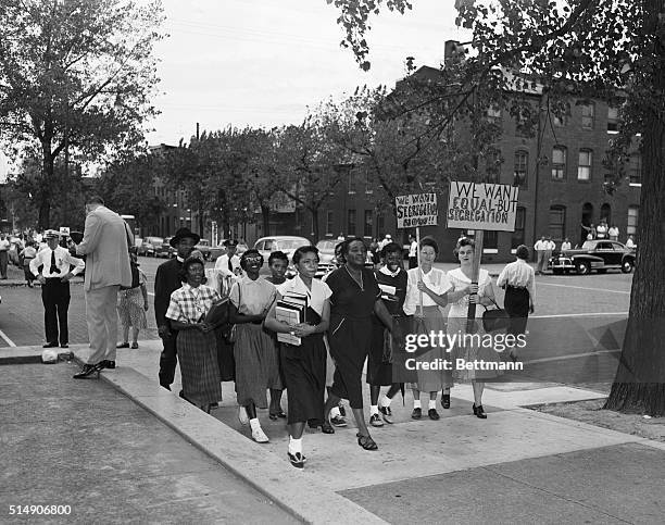 Police stand guard as a group of African American students, escorted by Reverend James L. Johnson, march past two demonstrators protesting...