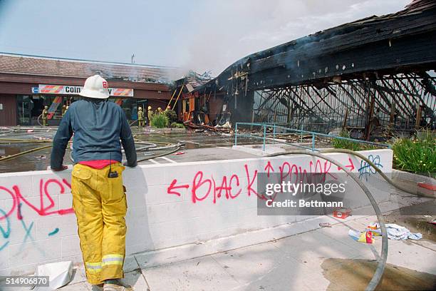 View, from behind, of a firefighter as he leans against a retaining wall and watches as colleagues extinguish a fire in a shopping center in the...