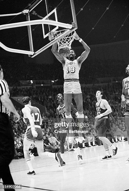 Big LA Laker center Wilt Chamberlain jumps to the rim of the basket to score, as Boston Celtics Tom sanders forward and Larry Siegried guard looks on...