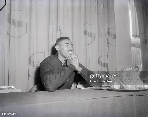 Wilt "The Stilt" Chamberlain of the University of Kansas is shown seated at a table with his hands crossed.