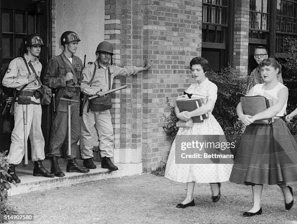 Young women students walk past members of the Arkansas National Guard, stationed there by Governor Orval Faubus to prevent nine African American high...