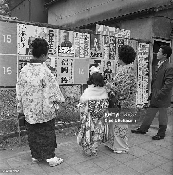 Tokyo, Japan-Kimono-clad young ladies try to decide which candidate to vote for in the general election as they gaze at these posters. With three...