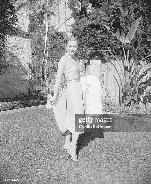 Full-length photo of Joan Fontaine standing on a lawn, with her coat over her arm.