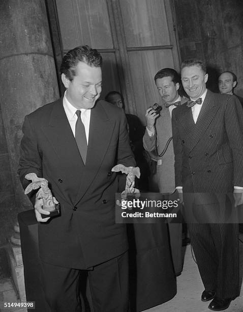 Orson Welles attending a Paris reception given by the Commerce Ministry for motion picture stars and directors, holds the two awards he received as...