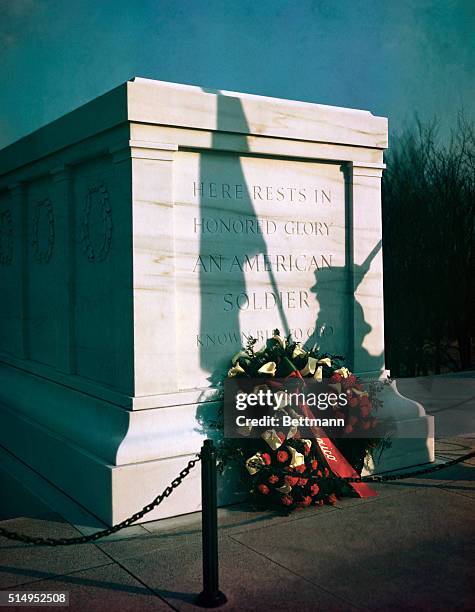 Wreath of flowers lays on the Tomb of the Unknown Soldier. There is a shadow of a soldier holding a US. Flag falling over the tomb.