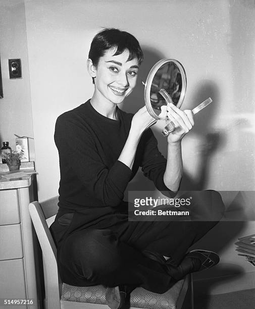 Audrey Hepburn holding a small hand mirror, in her dressing room at the 46th Street Theater,applies makeup for her role in the play Ondine. |...