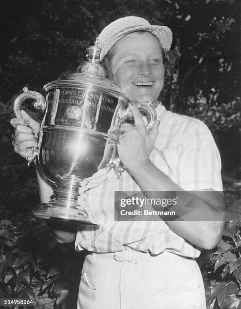 Babe Didrikson Zaharias grins and hugs the cup she received after becoming the first three-time winner of the U.S. Women's Open Golf Championship...