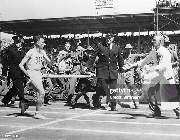 British runner Jim Peters staggers during the British Empire Games marathon, and Mickie Mayes , the English team's masseur, runs out on the track to...