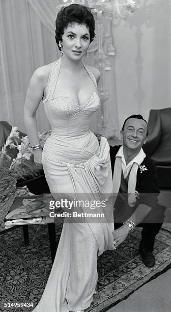 Beautiful Italian actress Gina Lollobrigida is shown with Emilio Shuberth in the gown he designed for her and which she will wear on the night of the...