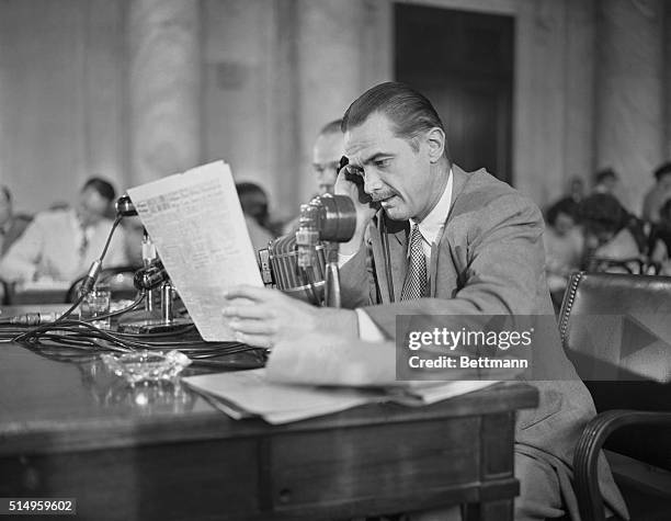 Partially deaf plane builder Howard Hughes shown using a special hearing aid provided by the Senate War Investigating Committee now probing his war...