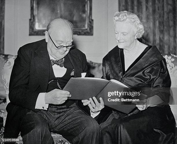 British Prime Minister Sir Winston Churchill and Lady Churchill admire the illuminated address, bound in a blue and gold leather cover, presented by...