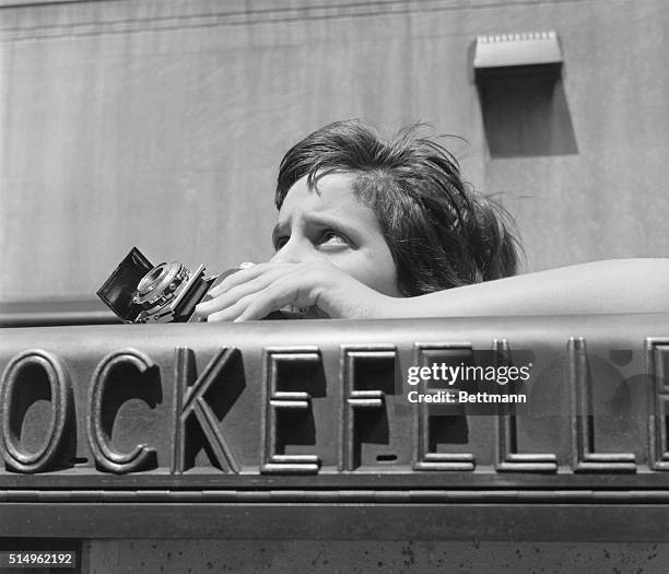 Girl trying to capture the Atlas statue at Rockefeller Center on film uses the top of a sign instead of a tripod to steady her camera.