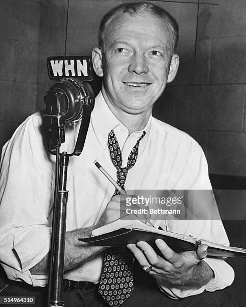 Walter "Red" Barber, sportscaster is shown writing as he is seated behind a microphone.