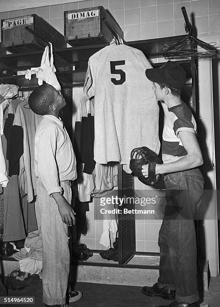Marvin Williams, 15 year old clubhouse boy, and Timmy Gray Yankee bat boy, gaze in youthful admiration at the uniform of Joe DiMaggio, hanging in the...