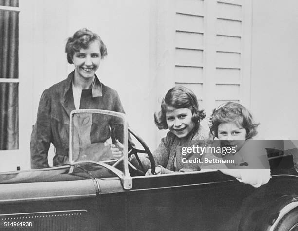 Princess Elizabeth and her younger sister Princess Margaret of Great Britain play in a miniature automobile while their governess, Marion Crawford,...