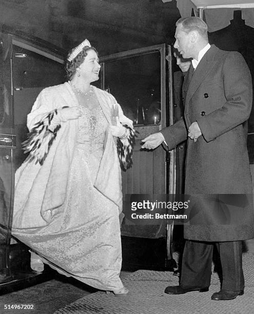 King George graciously assists his Queen, Elizabeth, from their automobile as they arrive at the London Coliseum to attend a royal command variety...
