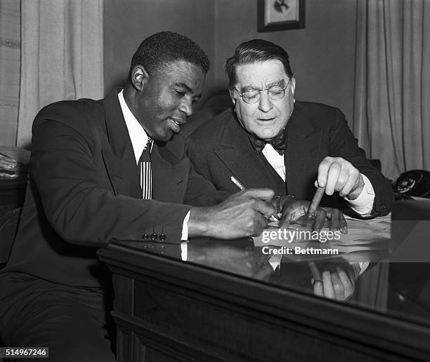 Brooklyn,NY: Jackie Robinson, the National League's MVP in 1949, is shown signing a Brooklyn Dodger contract today as President Branch Rickey...